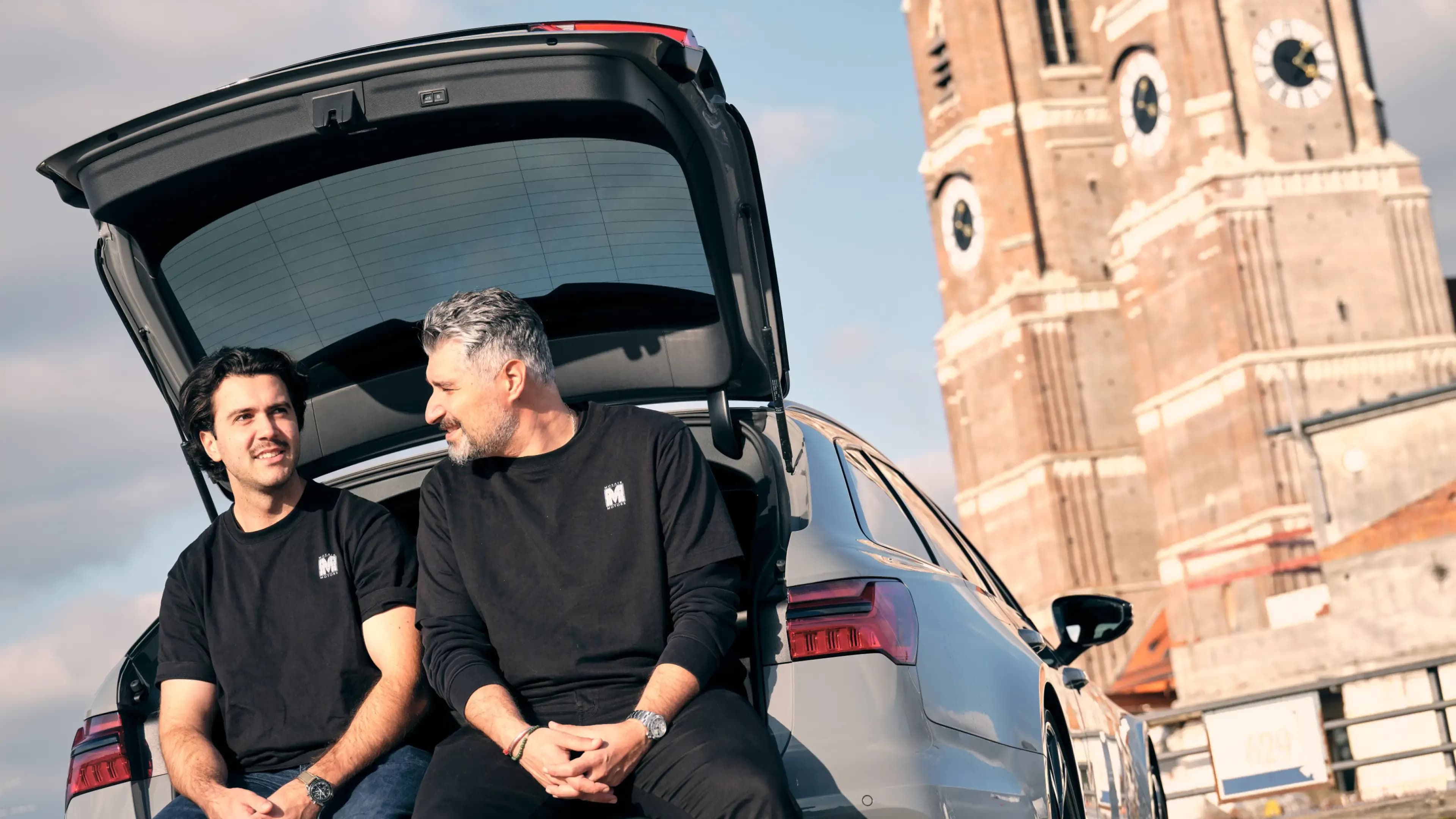 Mosaik Motors founders Lombardi Tomescu and Renan Serpen seated on a car boot in front of the iconic Frauenkirche in Munich.