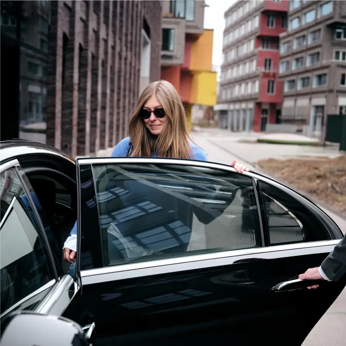 Exclusive chauffeur service Munich – a female customer stepping into a black luxury sedan with the door held open by a professional Mosaik Motors chauffeur.
