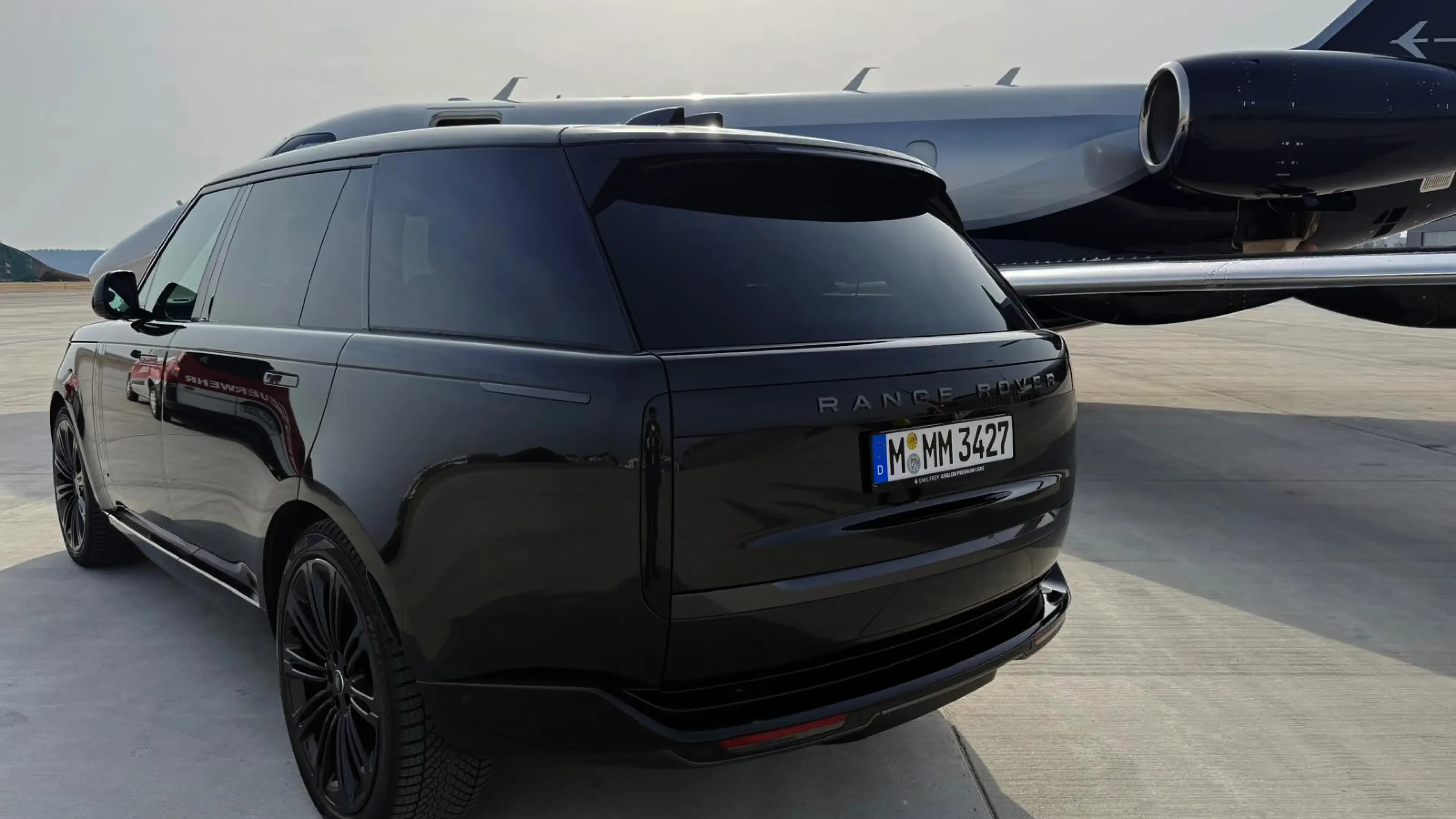 Range Rover Autobiography mieten in München – Heckansicht des Luxus-SUV in Santorini Black auf dem Flughafenvorfeld direkt neben einem Privatjet als Teil des exklusiven VIP-Flughafentransfer-Service von Mosaik Motors.