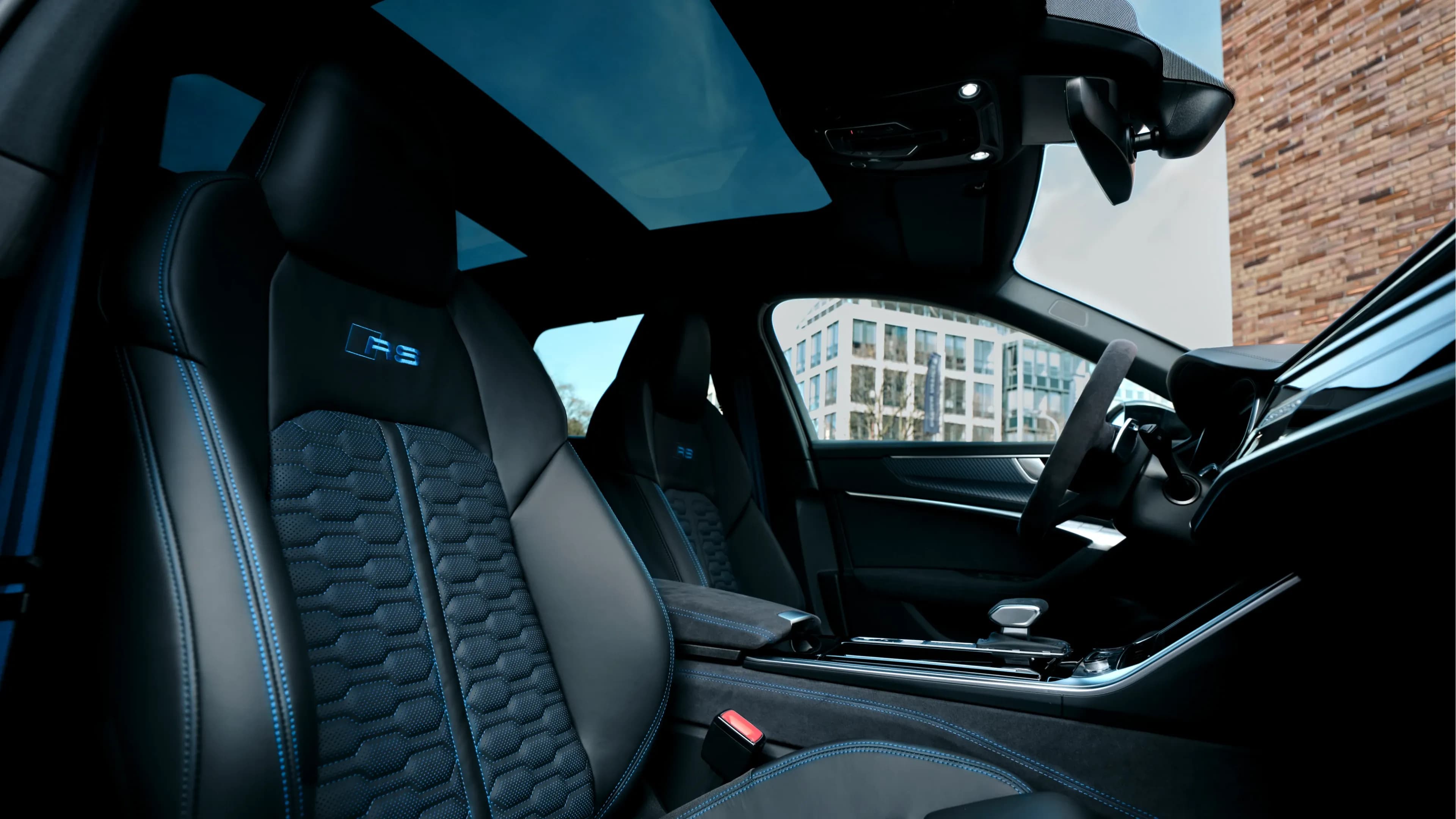 Audi RS6 Performance sport seats featuring blue contrast stitching and the RS logo under an open panoramic roof by Mosaik Motors.