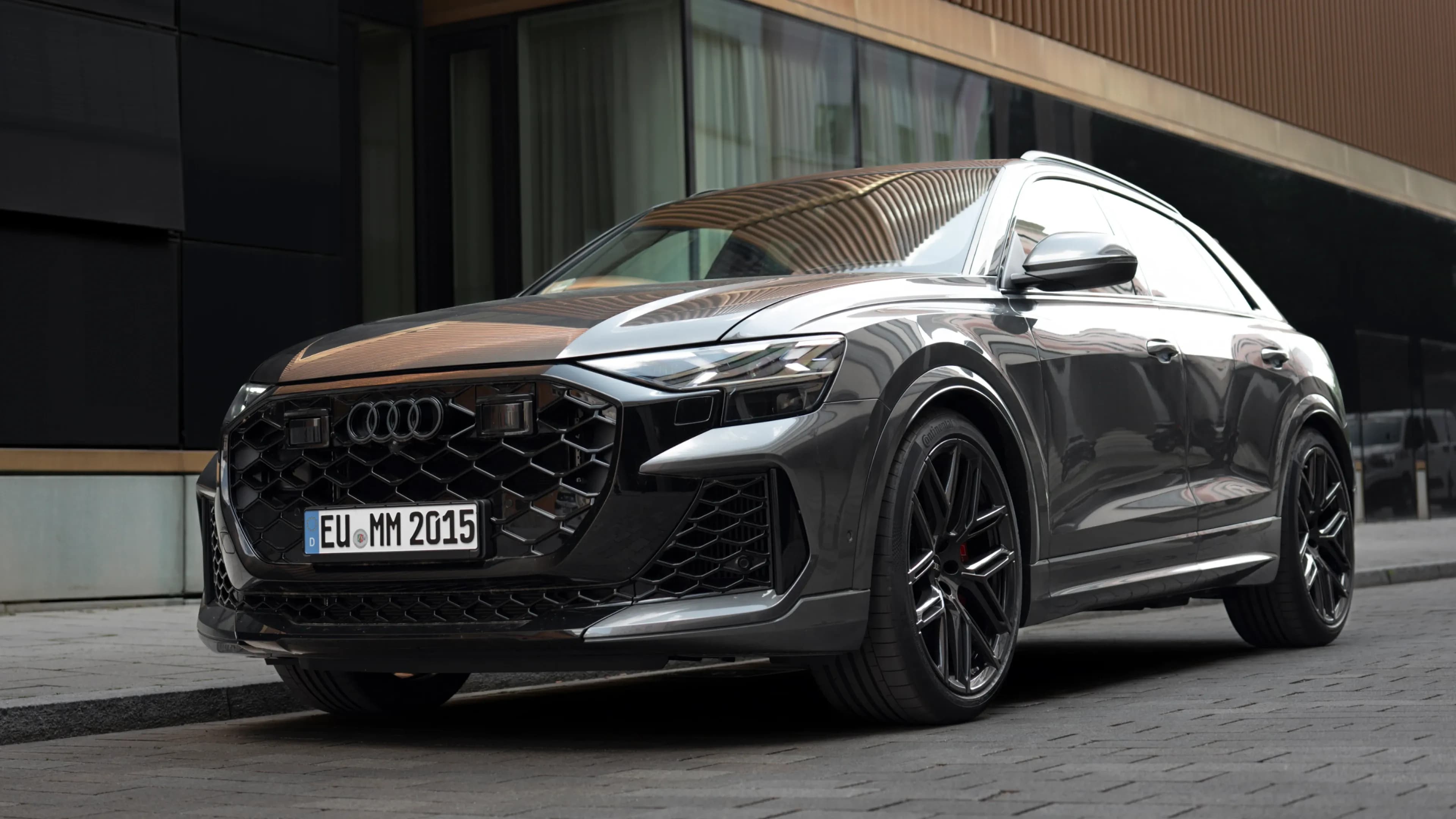Grauer Audi RS Q8 Avant in einer tiefen Dreiviertel-Frontansicht auf einer Münchner Kopfsteinpflasterstraße von Mosaik Motors.