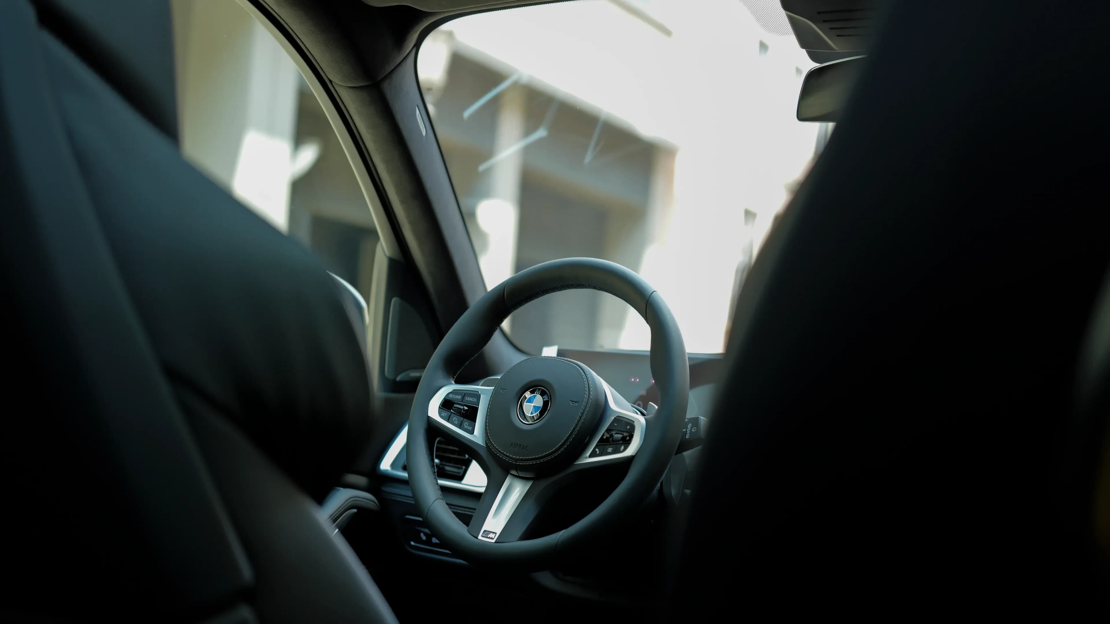 Elegantes BMW X7 M-Lederlenkrad mit Multifunktionstasten und Blick auf das digitale Cockpit-Display.