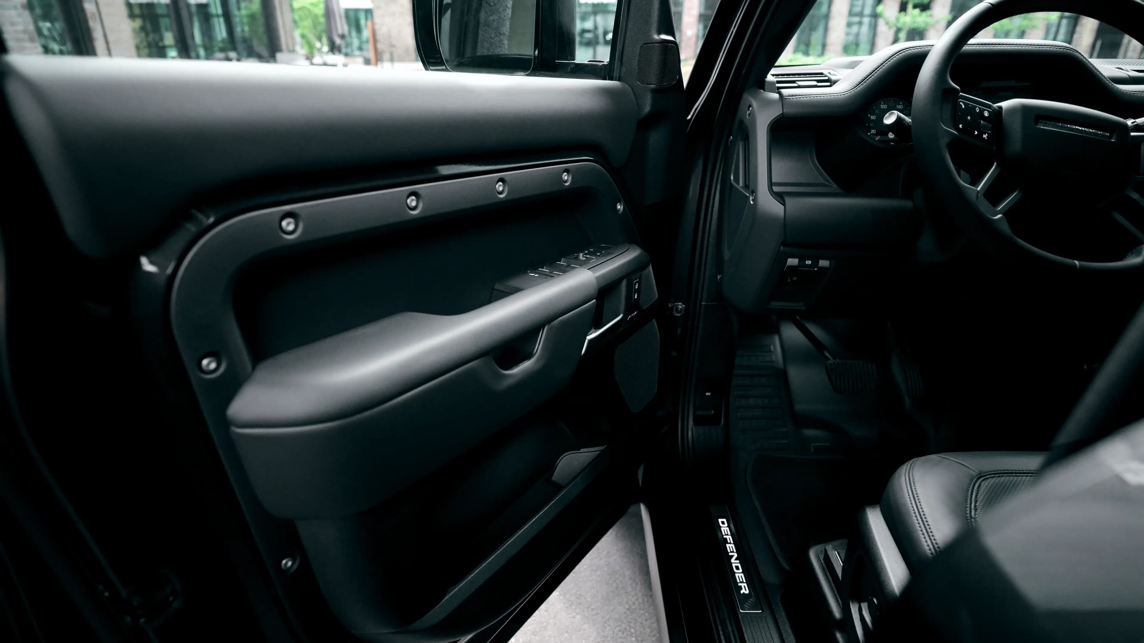 Innenansicht der Türverkleidung eines Land Rover Defender mit beleuchteter Defender-Einstiegsleiste und schwarzer Lederausstattung von Mosaik Motors.