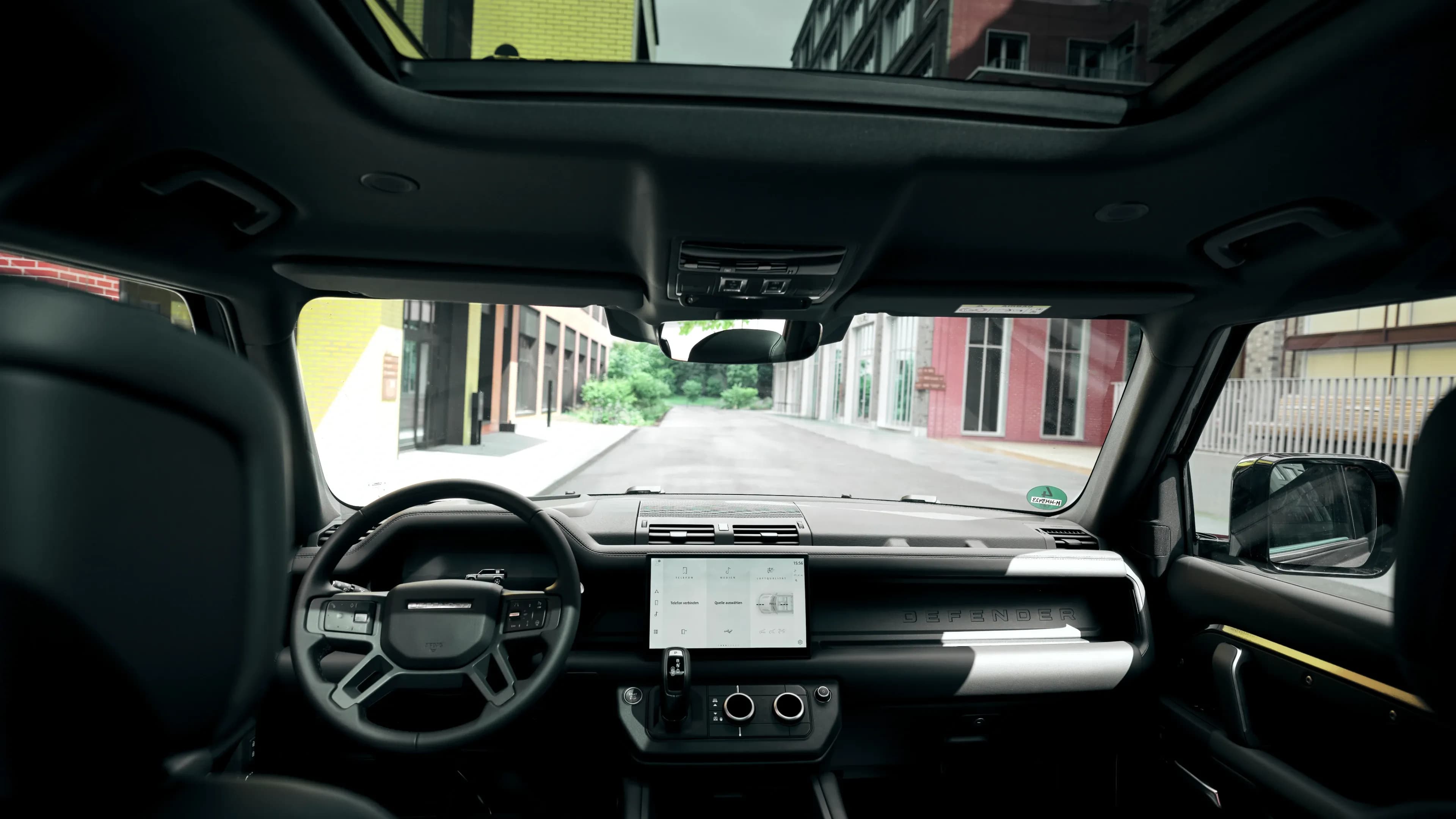 Innenansicht aus den Rücksitzen eines Land Rover Defender mit Blick auf das Panoramadach und den Dashboard-Touchscreen von Mosaik Motors.