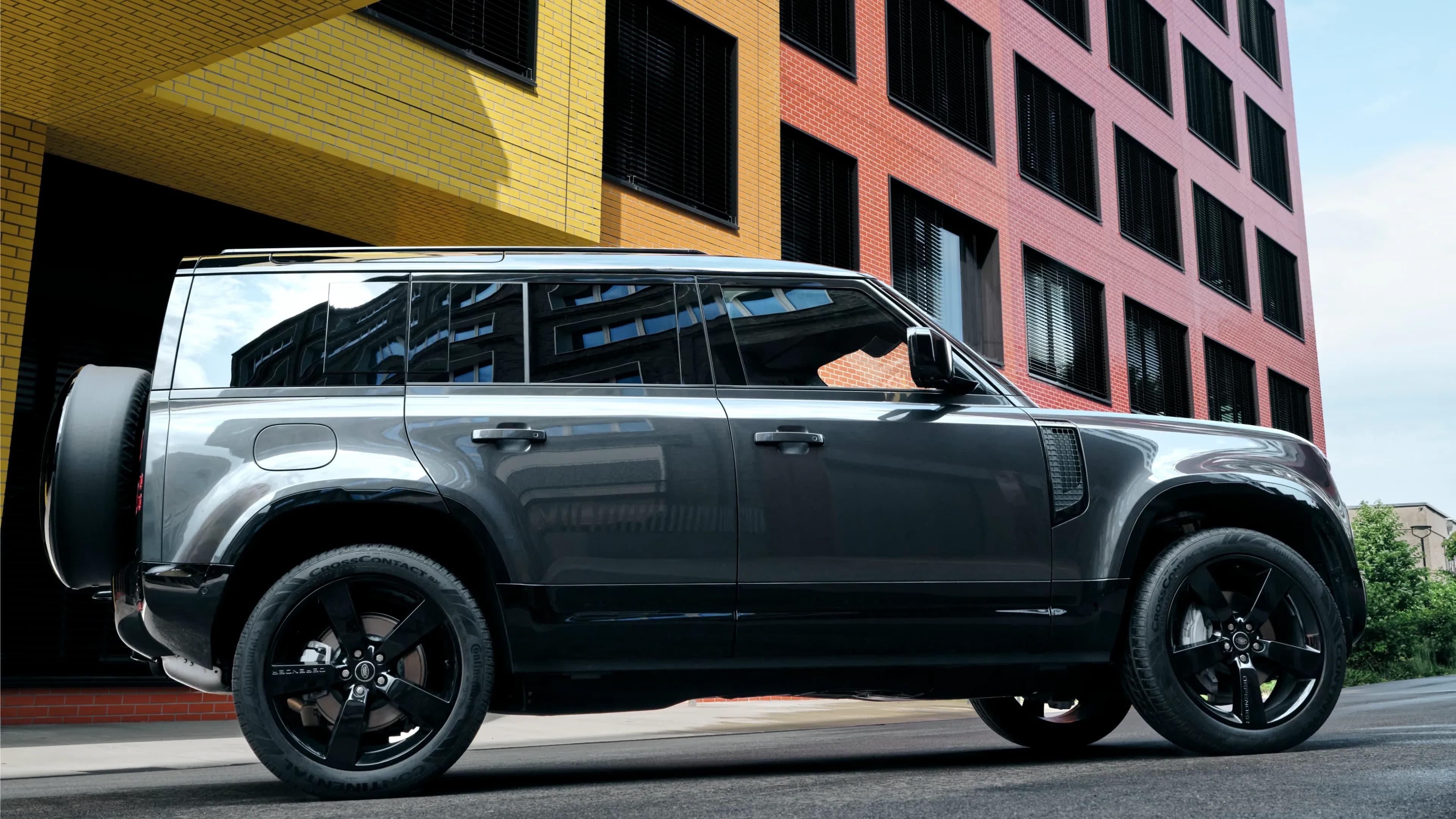 Side view of a grey Land Rover Defender 110 from Mosaik Motors in front of the colorful buildings at Design Offices Macherei in Munich.