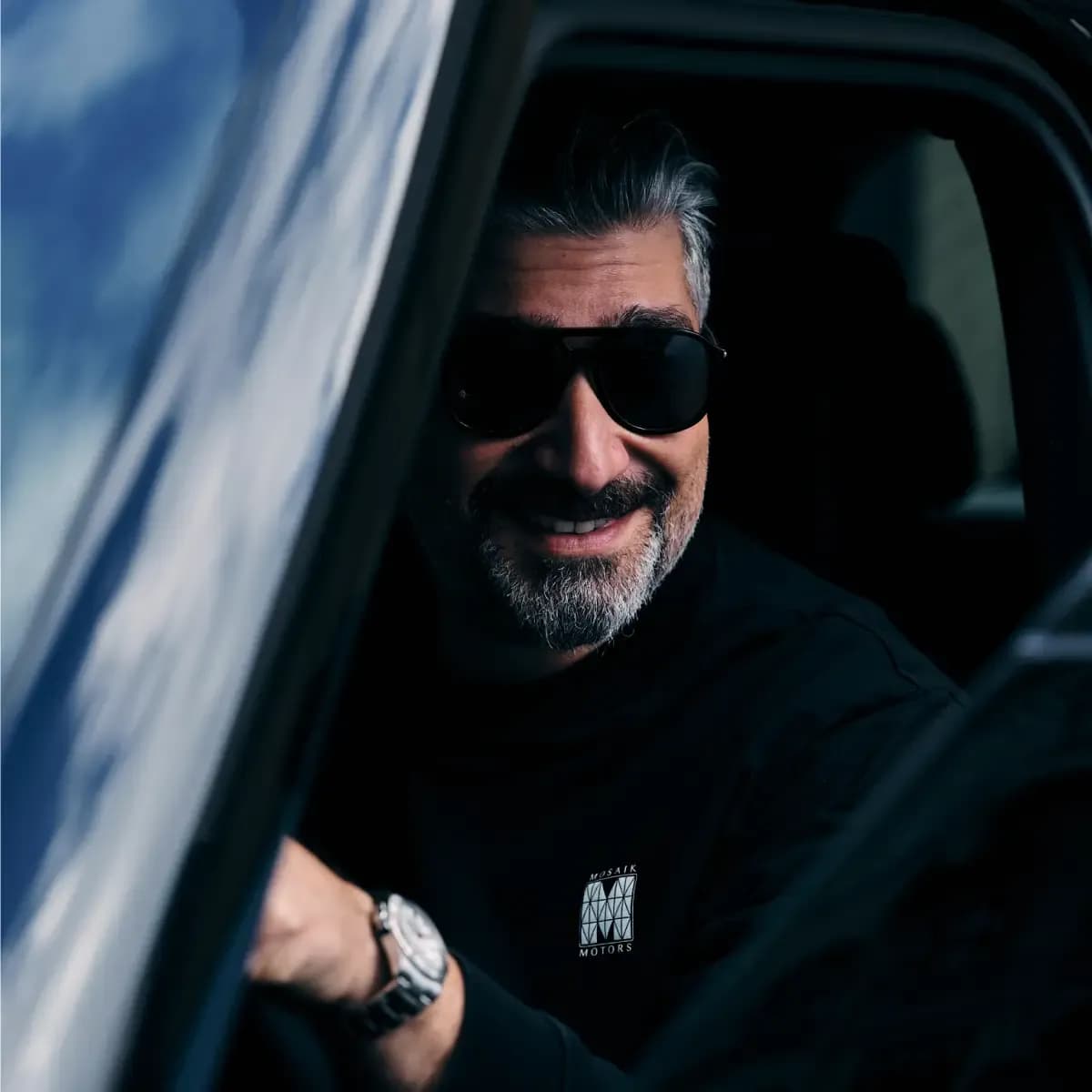 Renan Serpen, founder of Mosaik Motors luxury car rental Munich, seated inside a premium vehicle wearing sunglasses.